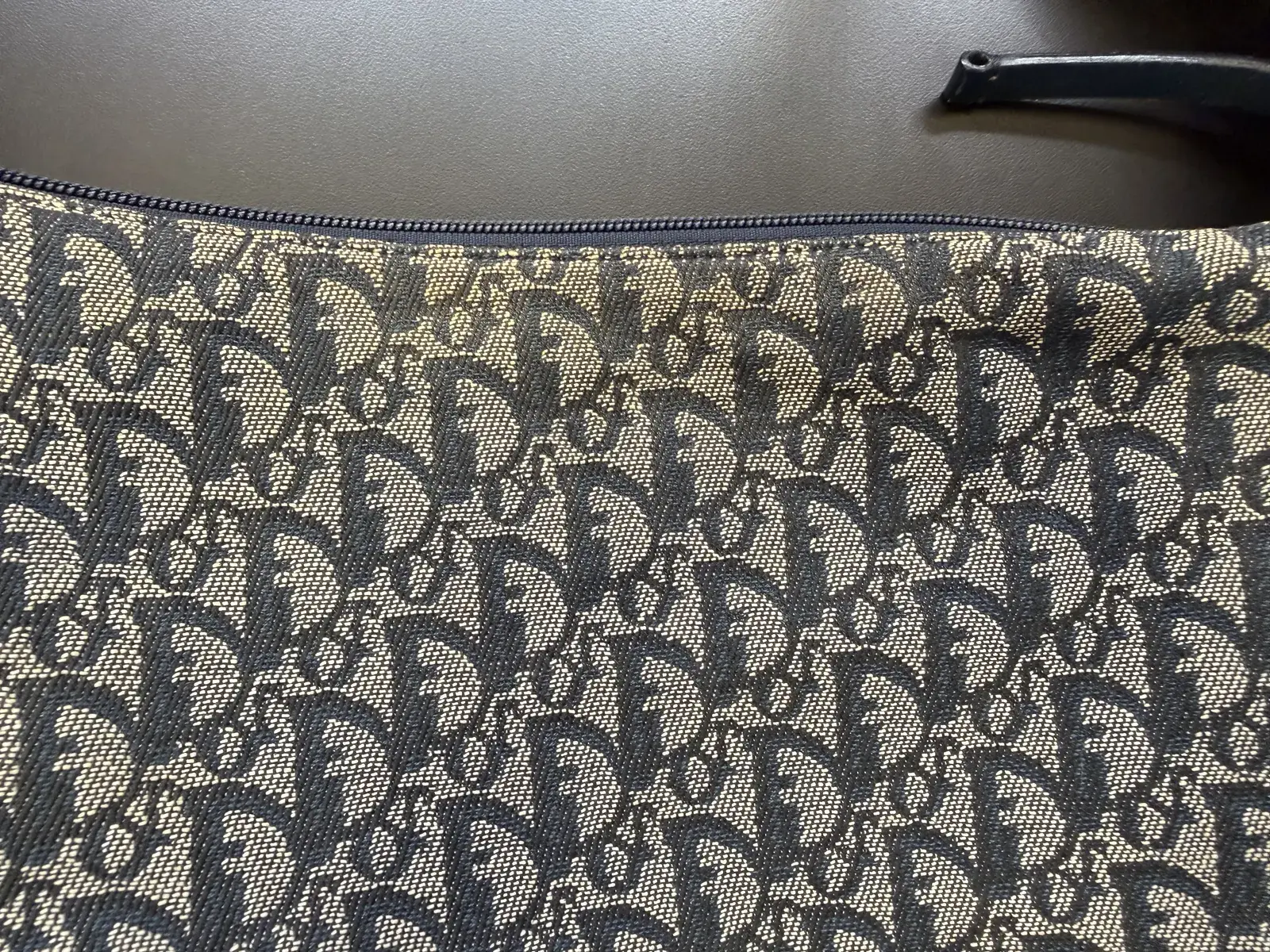 Close-up of the soiled band below the zipper on the Dior Trotter canvas bag before cleaning, the ecru Oblique pattern yellowed and grey
