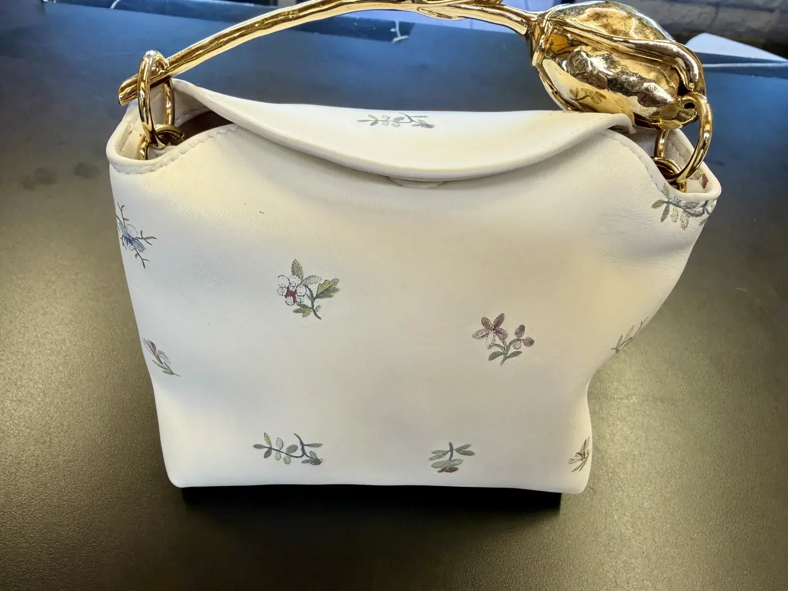 Close view of the Erdem Bloom gold toned flower bud brass handle above the cleaned white leather body