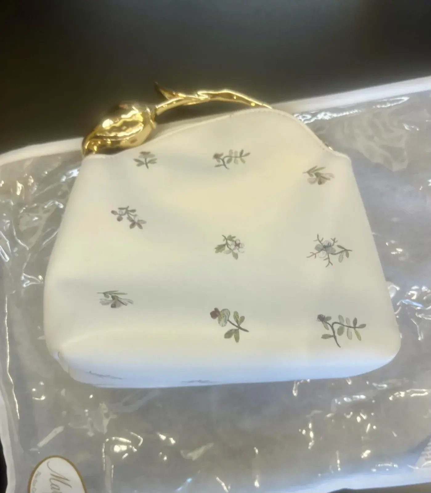 Erdem Mini Bloom tote at intake resting on its storage pouch, white leather with delicate floral print and gold flower bud handle