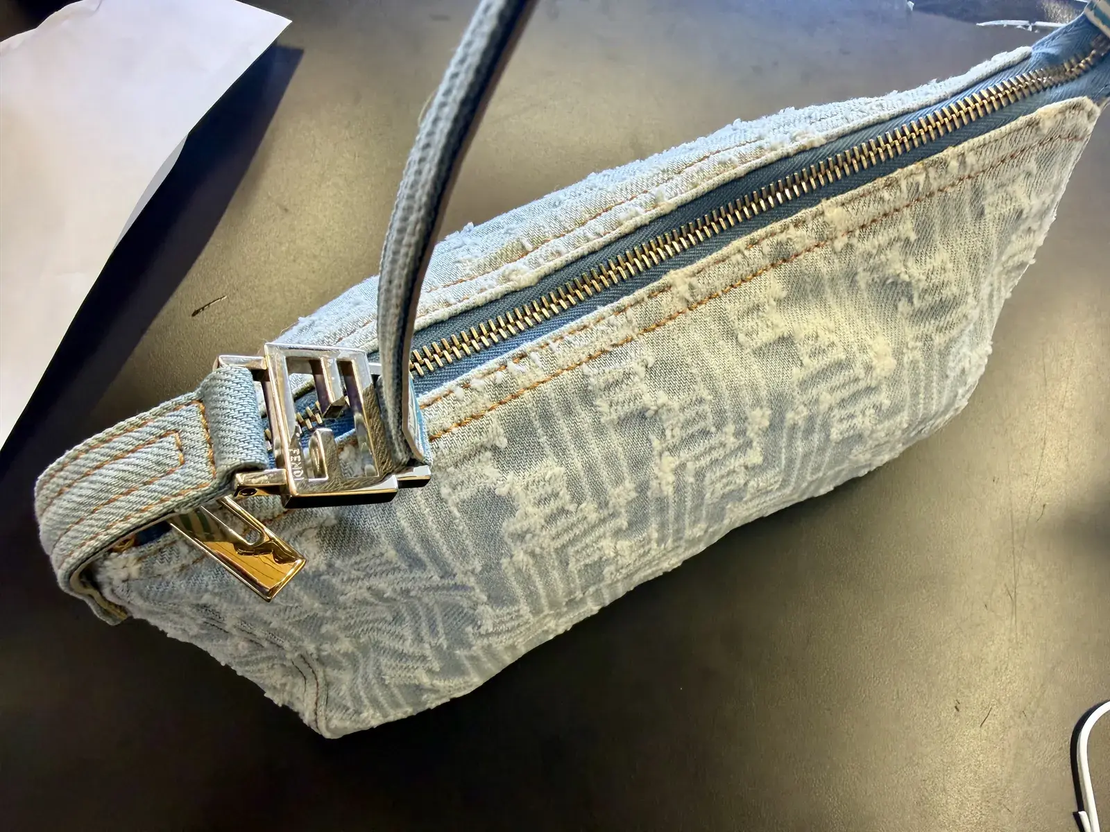 Angled view of the cleaned Fendi denim bag showing the polished FF strap buckle and gold toned zipper end against clean distressed denim