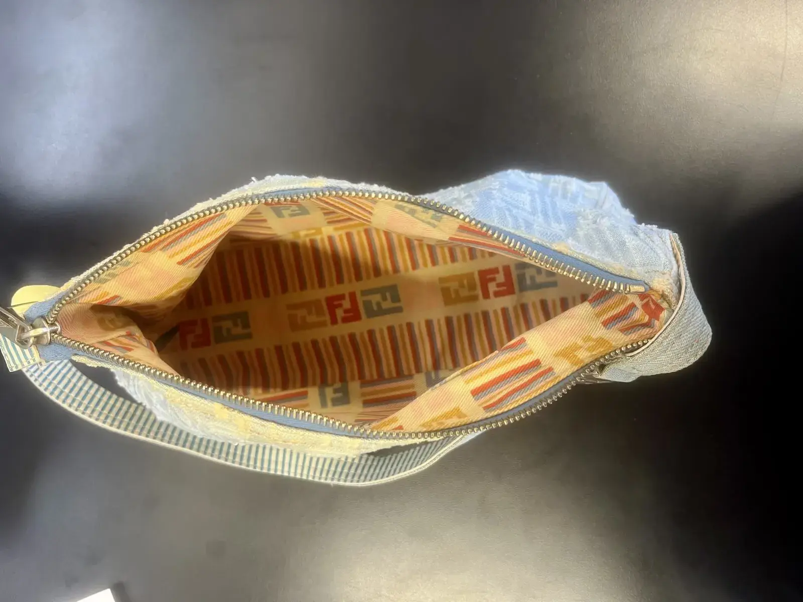 Inside the Fendi bag before cleaning, the multicolor striped FF logo lining soiled and dull with the denim exterior yellowed around the zipper