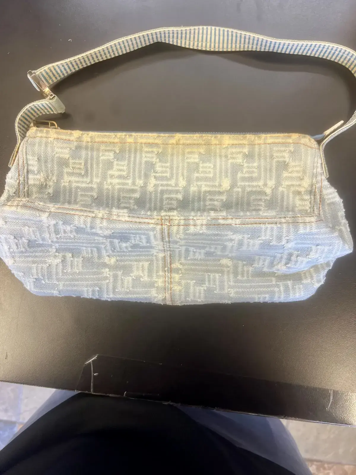 Fendi denim bag at intake with its striped canvas shoulder strap, the yellow discoloration visible along the zipper line and the front panel