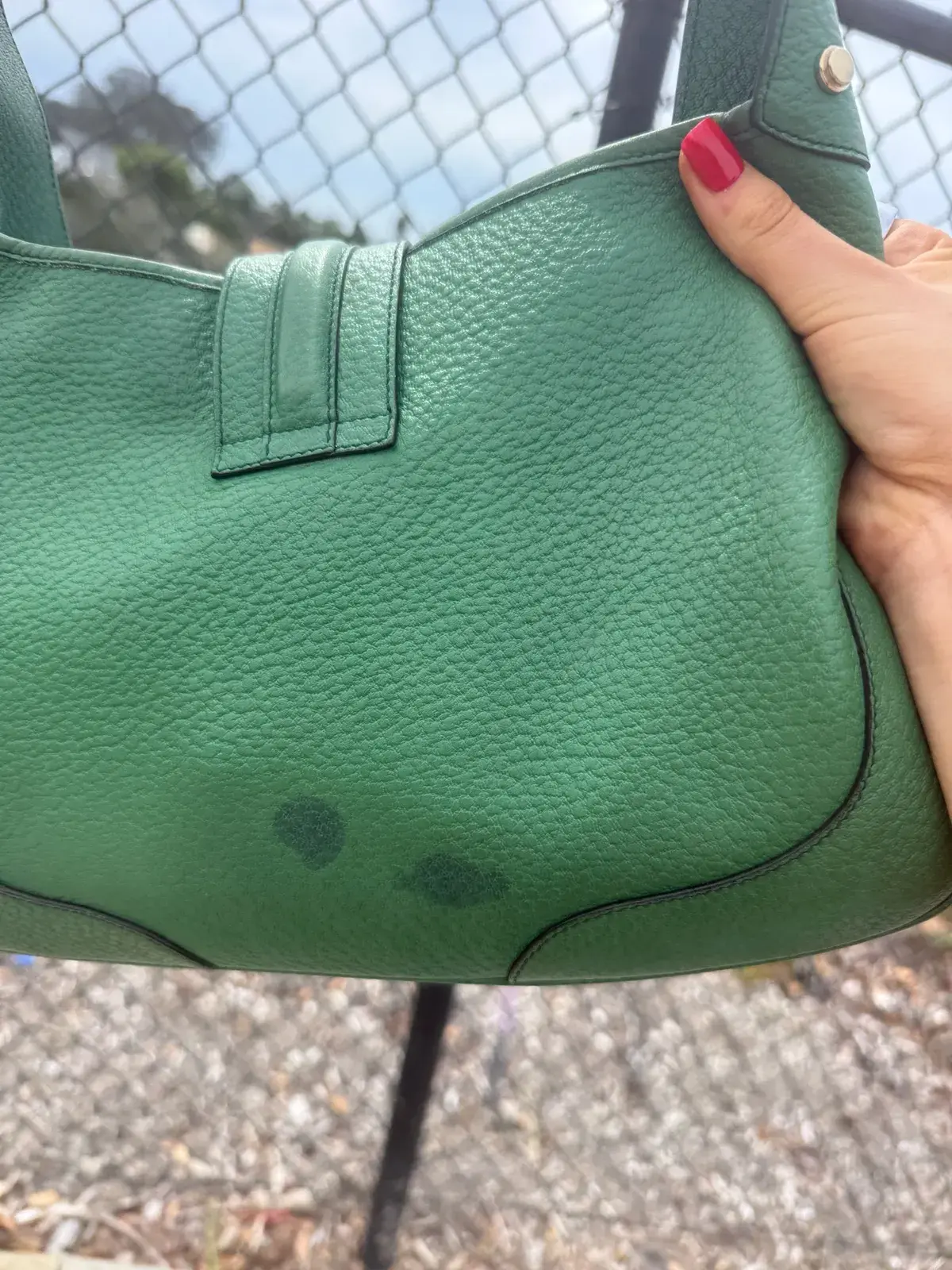 Back of the green leather Gucci Jackie before cleaning, two dark green oil spots on the lower panel from a vitamin softgel that broke inside the bag