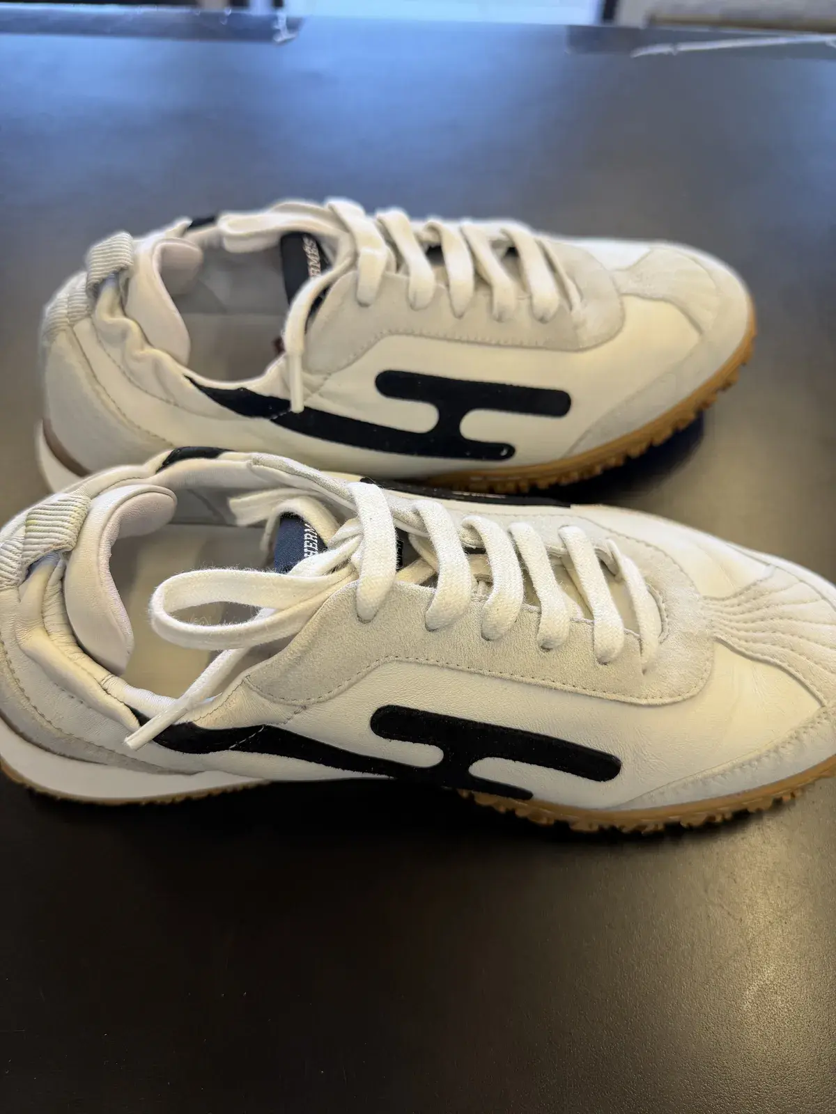 Cleaned Hermes leather sneakers photographed at an angle, white uppers and crisp black H side logo restored