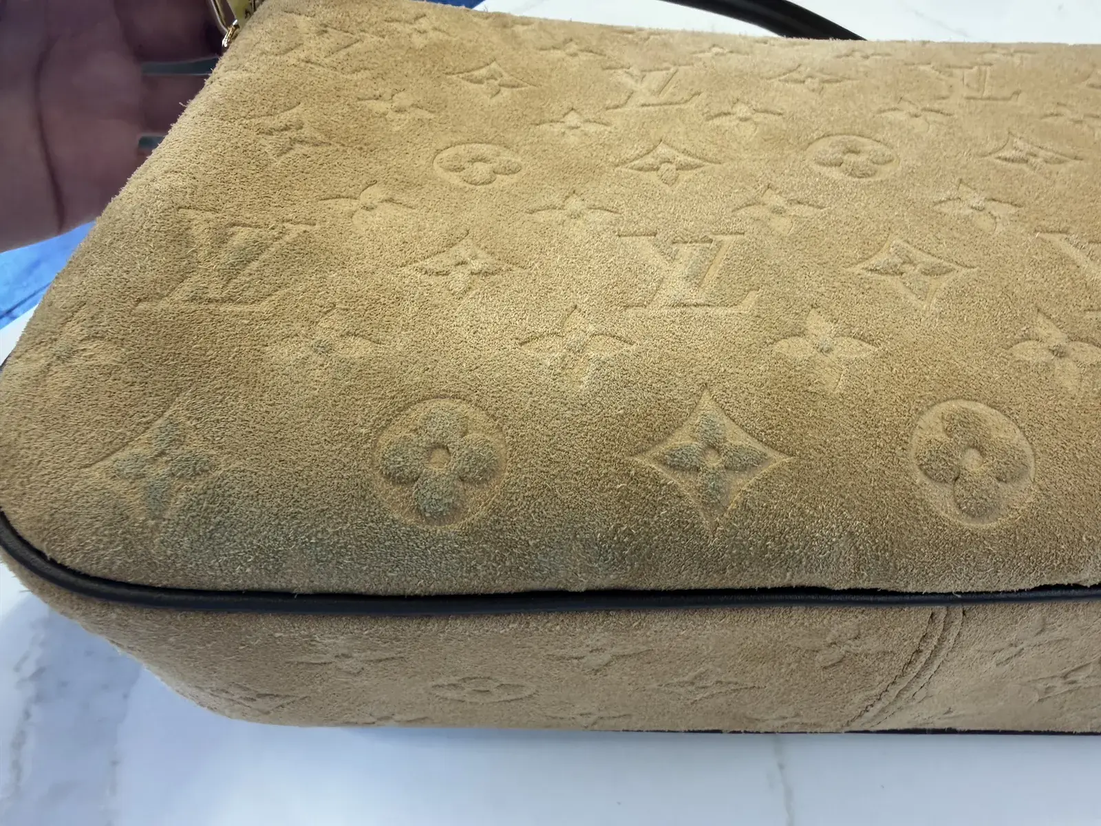 Lower edge of the Louis Vuitton suede Pochette Métis Soft MM flap before cleaning, blue-grey dye transfer marking the embossed Monogram above the Chocolate piping