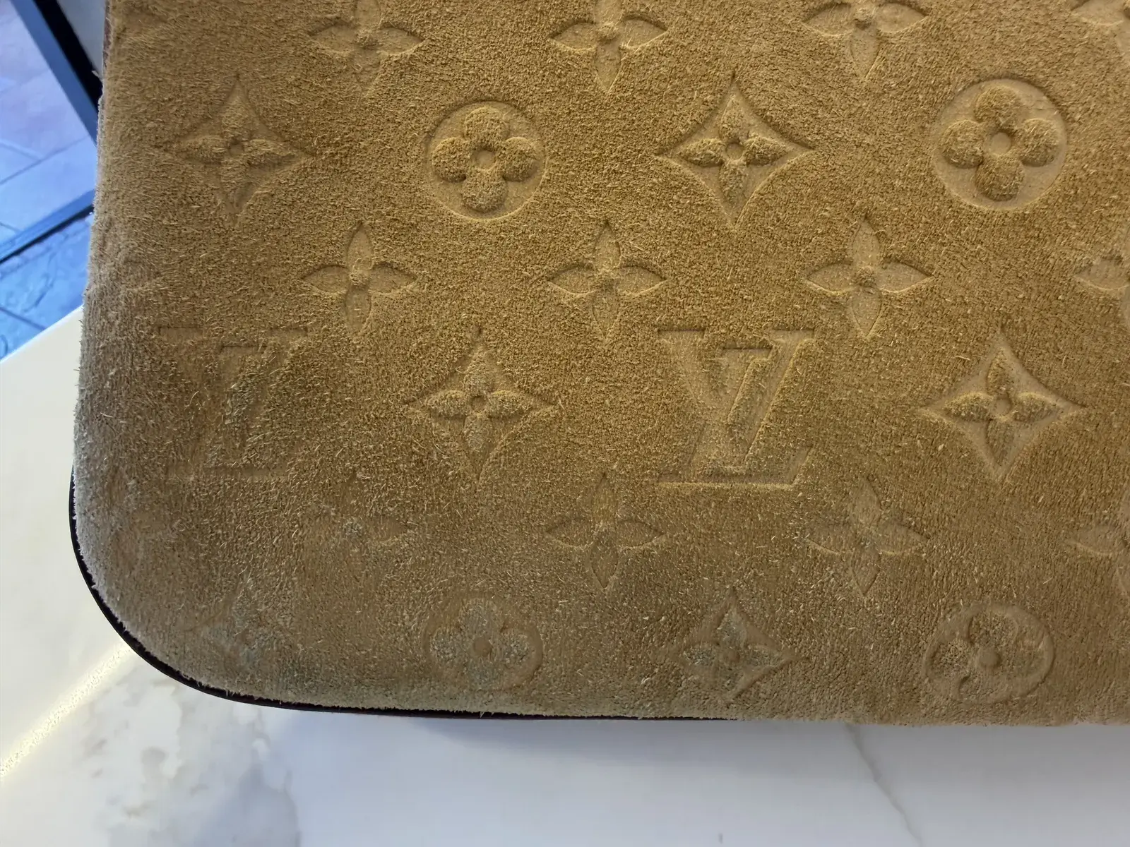 Close-up of the Louis Vuitton suede bag before cleaning, blue-grey dye transfer from a new shirt sitting in the embossed Monogram flowers near the lower corner